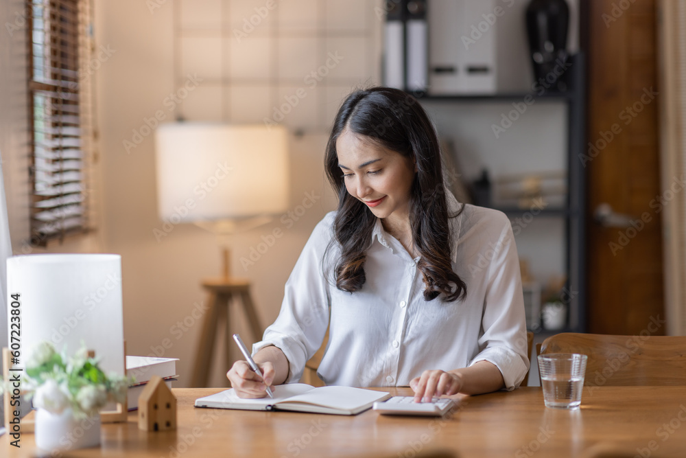 Young adult happy smiling business asuan woman working on desk home office with using a calculator to calculate the numbers, finance accounting business educationconcept Young adult happy smiling business asuan woman working on desk home office with using a calculator to calculate the numbers, finance accounting business educationconcept