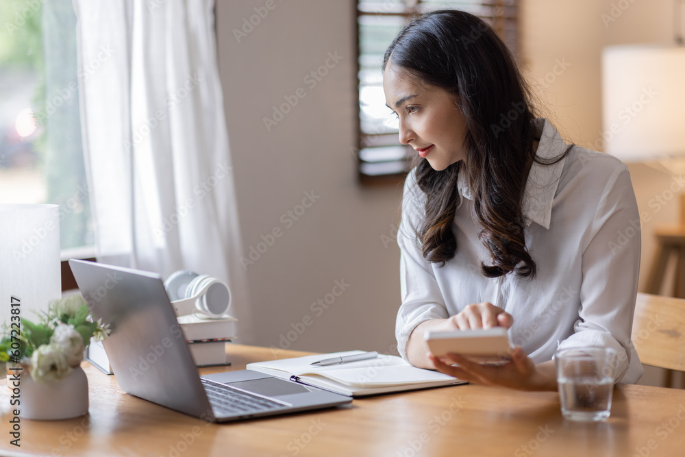 Young adult happy smiling business asuan woman working on desk home office with using a calculator to calculate the numbers, finance accounting business educationconcept Young adult happy smiling business asuan woman working on desk home office with using a calculator to calculate the numbers, finance accounting business educationconcept