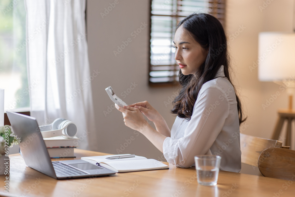 Young adult happy smiling business asuan woman working on desk home office with using a calculator to calculate the numbers, finance accounting business educationconcept Young adult happy smiling business asuan woman working on desk home office with using a calculator to calculate the numbers, finance accounting business educationconcept