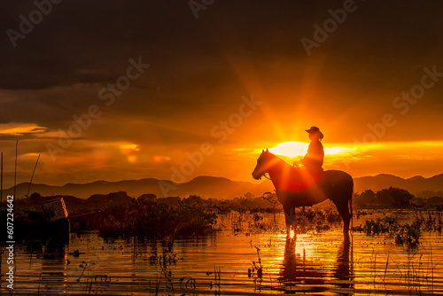 Silhouette the cowboy riding on a mountain with an yellow sky; Concept of friendly and of summer vacation.