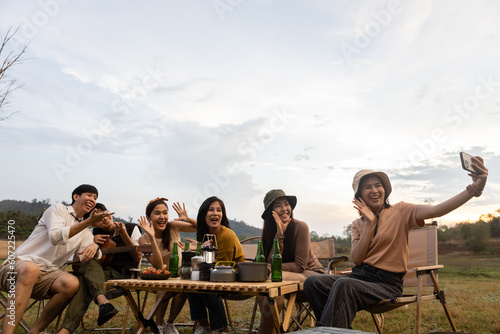 Group of young asian people camping vacation on countryside. Tourist using smartphone selfie camera photo in camping. Happy holiday trip.