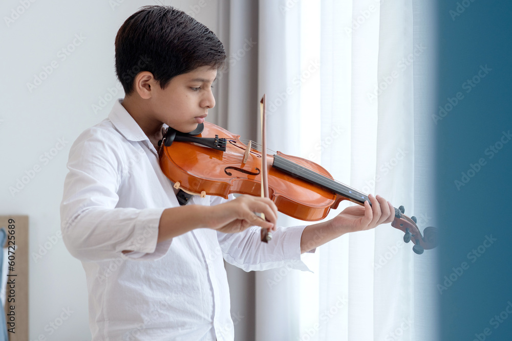Indian teenage boy playing and practicing violin, classical music instrument at home, musical education concept