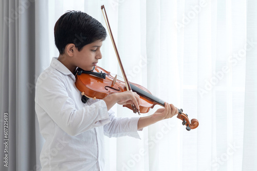 Indian teenage boy playing and practicing violin, classical music instrument at home, musical education concept