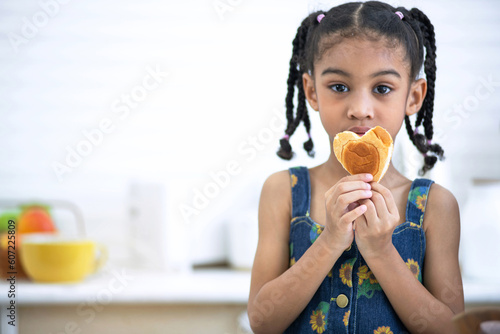 Cute little girl showing heart-shaped bread in hand at kitchen