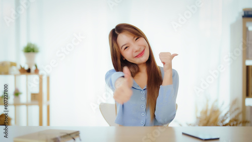 Happy teen asian girl blogger smiling face waving hand talking to webcam recording vlog, social media influencer streaming, making video call at home. She thumb up good or better