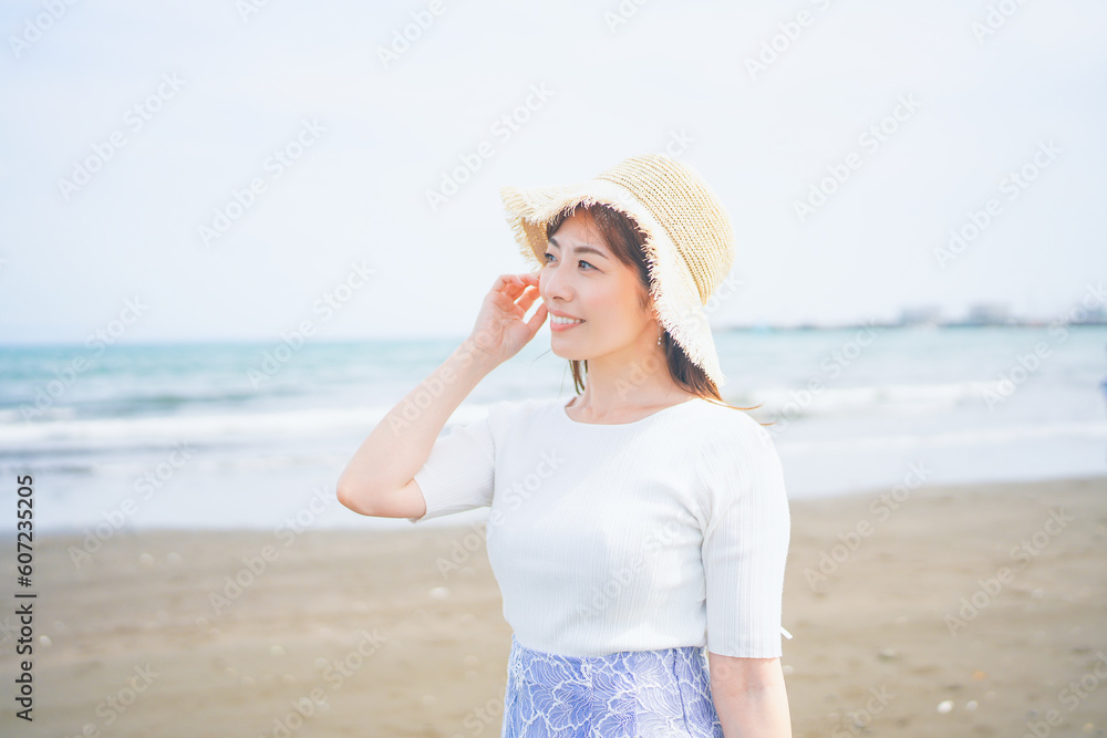 海で潮風を感じる麦わら帽子を被った笑顔の女性 海で潮風を感じる麦わら帽子を被った笑顔の女性