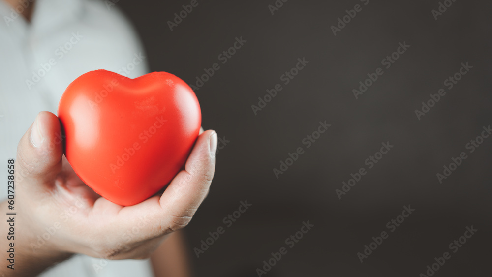 Man holding a red heart shape while standing with black background in the studio. Space for text. Donate, love, and encouragement concept Man holding a red heart shape while standing with black background in the studio. Space for text. Donate, love, and encouragement concept
