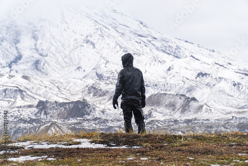 A man stands alone against the backdrop of a large mountain. Bad weather