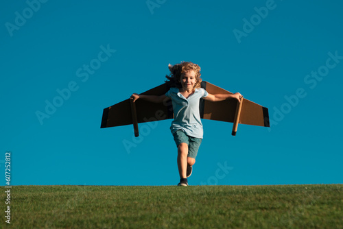 Kid playing with toy plane wings in summer park. Kid dreams of future. Kid pilot dreaming. Childhood dream concept. Blonde cute daydreamer child dream on fly. Creative kid. photo