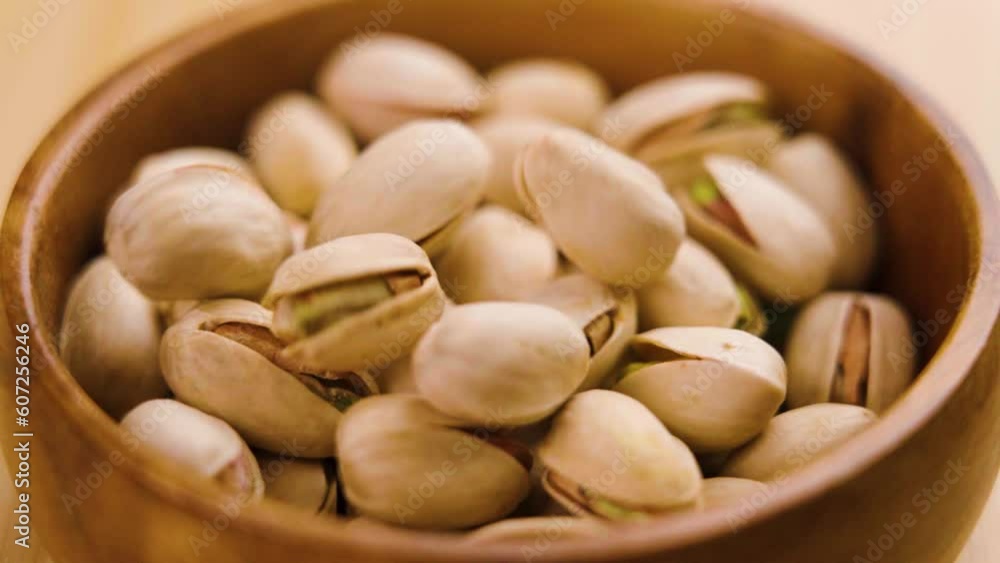 Dried pistachio nuts with cracked shells and green kernels falling into a rustic wooden bowl closeup Dried pistachio nuts with cracked shells and green kernels falling into a rustic wooden bowl closeup