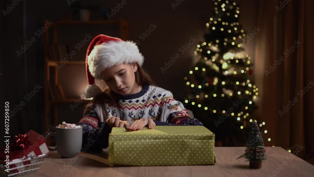 Teenage girl is wrapping a Christmas gift in paper while sitting at table home on Christmas Eve. Teenage girl is wrapping a Christmas gift in paper while sitting at table home on Christmas Eve.
