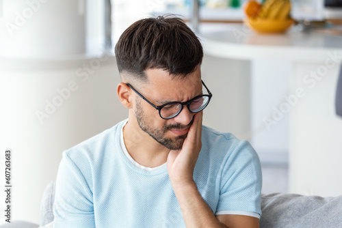 Depressed ill man having toothache and touching cheek. Young man suffering from tooth pain, caries. Male suffering from toothache, closeup. Portrait of casual man toothache with painful expression