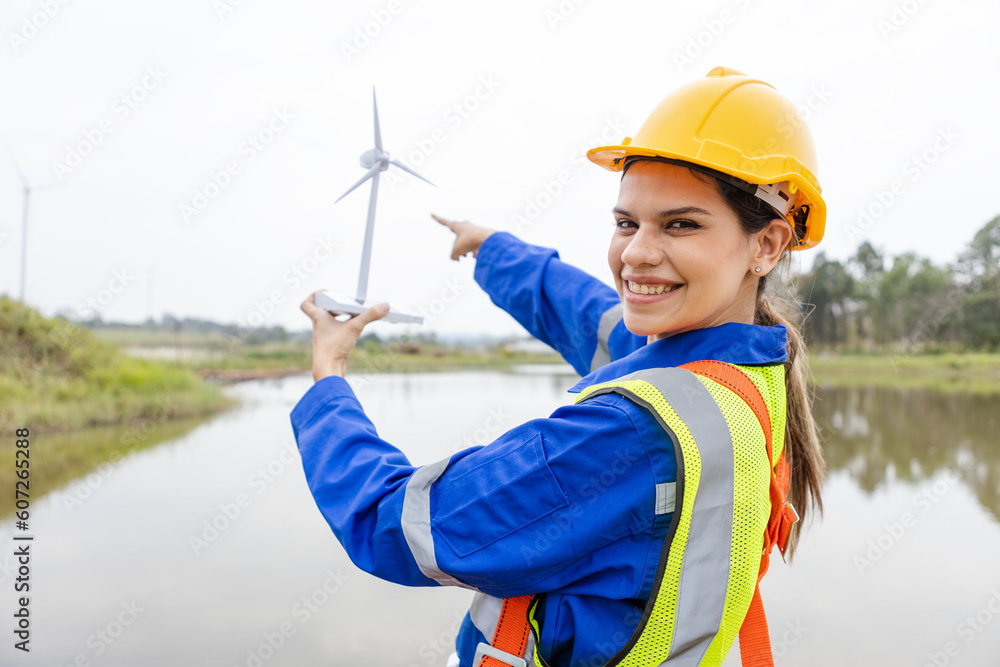 Smiling female engineer of wind turbine energy company. woman pointing forward at station energy power wind. technology protect environment reduce global warming problems. Innovative renewable energy. Smiling female engineer of wind turbine energy company. woman pointing forward at station energy power wind. technology protect environment reduce global warming problems. Innovative renewable energy.