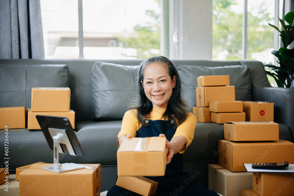 Mature business owner woman prepare parcel box and standing check online orders for deliver to customer on tablet, laptop Shopping Online Mature business owner woman prepare parcel box and standing check online orders for deliver to customer on tablet, laptop Shopping Online