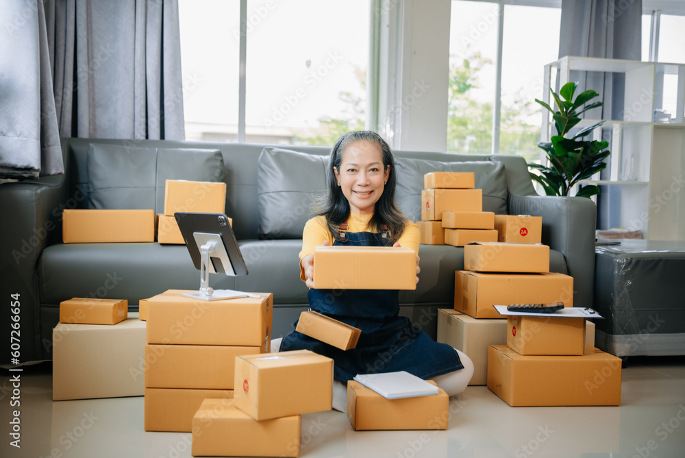 Mature business owner woman prepare parcel box and standing check online orders for deliver to customer on tablet, laptop Shopping Online Mature business owner woman prepare parcel box and standing check online orders for deliver to customer on tablet, laptop Shopping Online