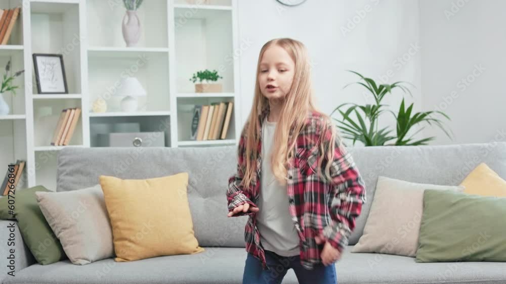 Artistic caucasian girl dancing briskly then jumping and falling on couch. Casually dressed dynamic kid having fun indoors and enjoying school holidays. Concept of active leisure activity at home. Artistic caucasian girl dancing briskly then jumping and falling on couch. Casually dressed dynamic kid having fun indoors and enjoying school holidays. Concept of active leisure activity at home.