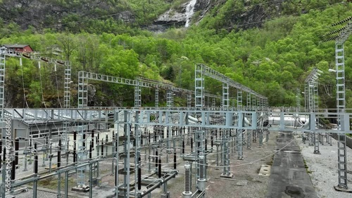 High voltage electrical power distribution centre outside hydroelectric powerstation with a symbolic renewable waterfall revealed in background - Aerial with tilt up - Matre Norway photo