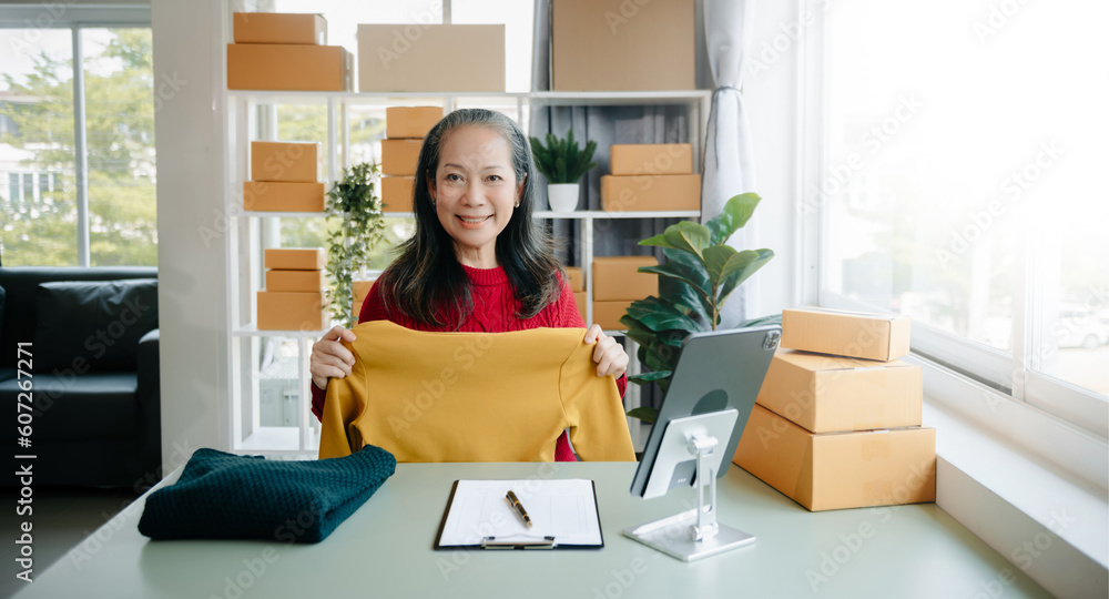 Mature business owner woman prepare parcel box and standing check online orders for deliver to customer on tablet, laptop Shopping Online Mature business owner woman prepare parcel box and standing check online orders for deliver to customer on tablet, laptop Shopping Online