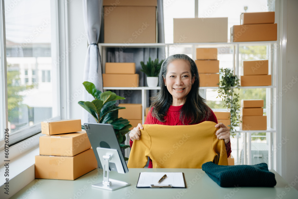 Mature business owner woman prepare parcel box and standing check online orders for deliver to customer on tablet, laptop Shopping Online Mature business owner woman prepare parcel box and standing check online orders for deliver to customer on tablet, laptop Shopping Online