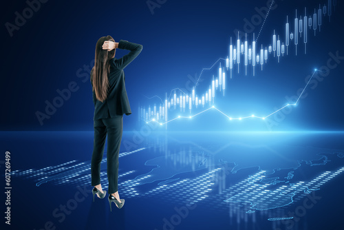 Back view of thoughtful young european businesswoman with creative candlestick forex chart or graph on blue background. Financial trade market and stock concept.