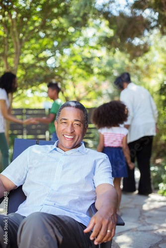 Portrait of smiling senior man on patio with family in background