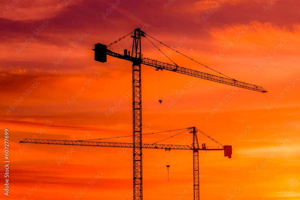 Silhouette of construction cranes against vivid orange sunset sky