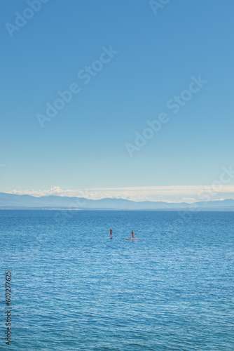 Unrecognizable people stand-up paddle boarding at Adriatic sea Kvarner gulf seen from the Lovran town coastline