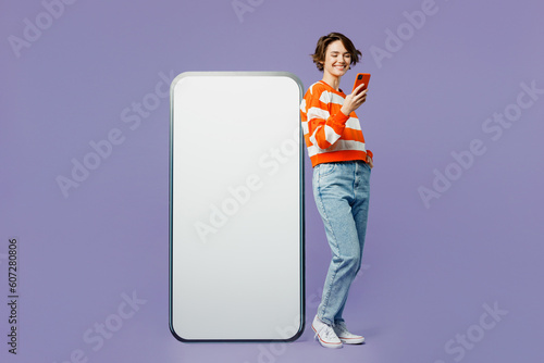 Full body fun young woman she wear casual clothes sweatshirt big huge blank screen mobile cell phone smartphone with mockup area use mobile cell phone isolated on plain pastel light purple background.