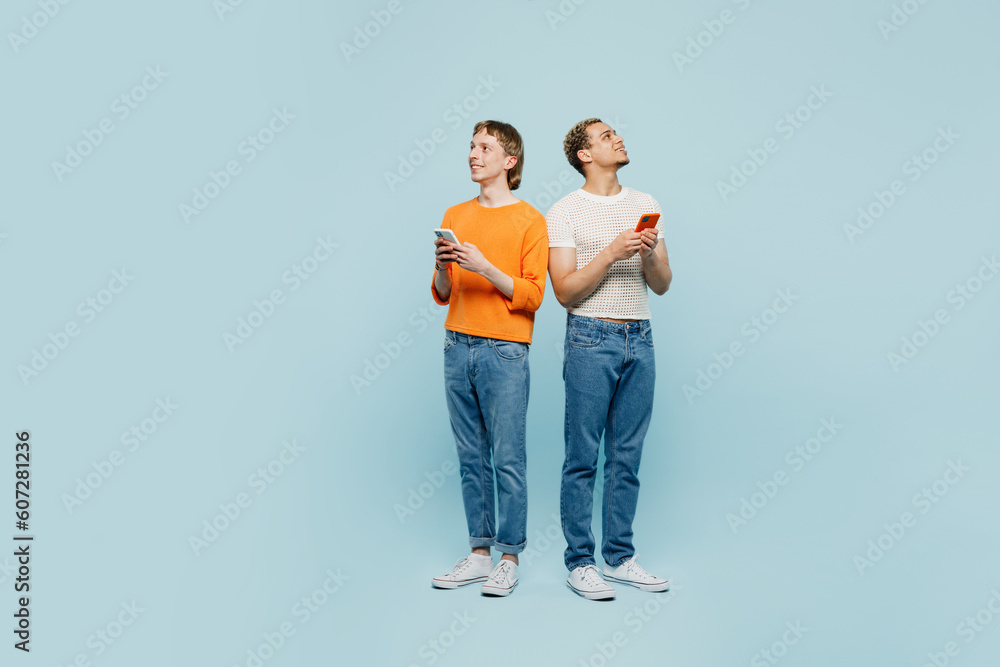 Full body fun young couple two gay men wear casual clothes together hold use mobile cell phone look aside isolated on pastel plain blue color background studio Pride day june month love LGBTQ concept. Full body fun young couple two gay men wear casual clothes together hold use mobile cell phone look aside isolated on pastel plain blue color background studio Pride day june month love LGBTQ concept.