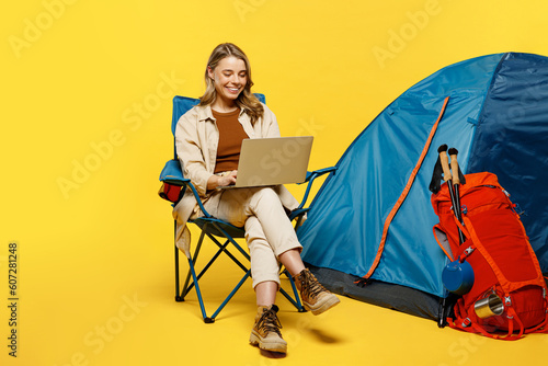 Full body young IT woman sit near bag with stuff tent work use laptop pc computer browse internet isolated on plain yellow background. Tourist walk on spare time. Hiking trek rest travel trip concept. #607281248