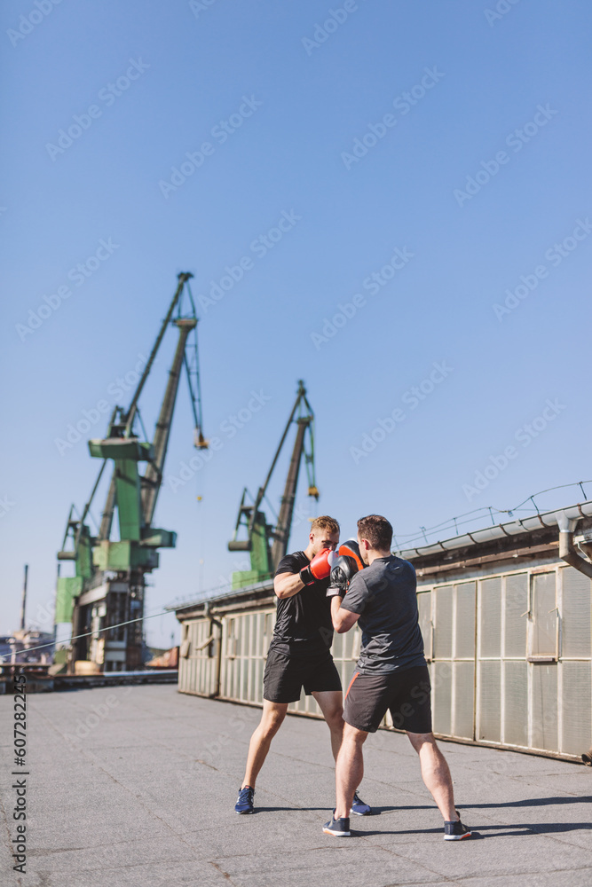 Fototapeta premium Two men do boxing training on roof of the building in industrial city