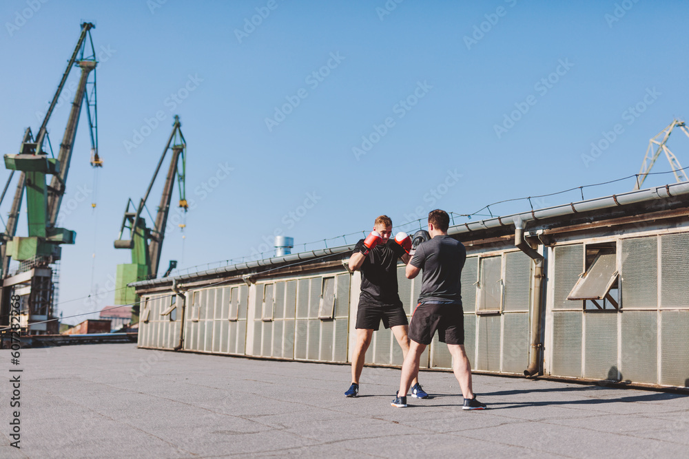 Two men do boxing training on roof of the building in industrial city