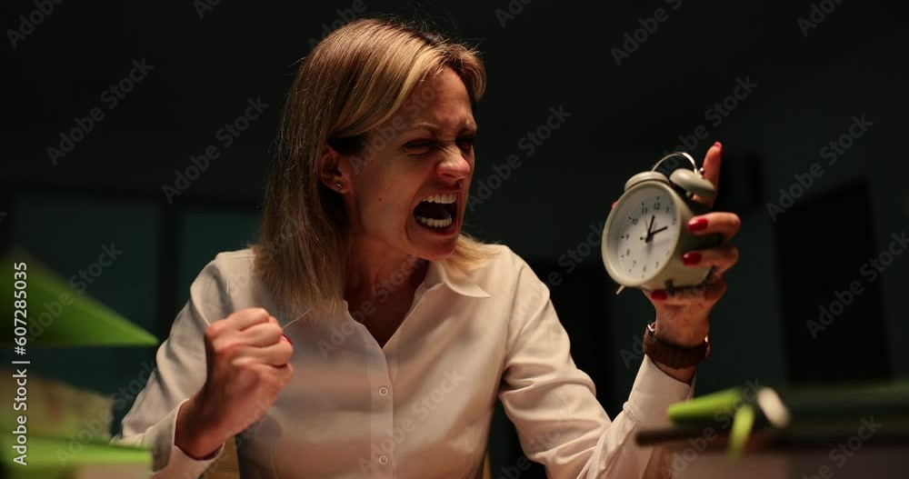 Manager screams holding an alarm clock sitting working in office in
