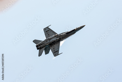 Bottom view of a hornet F-16 jet fighter in Gijon Air show festival doing tricks at subsonic speed in a clear summer blue sky with condensation big steles in its wings