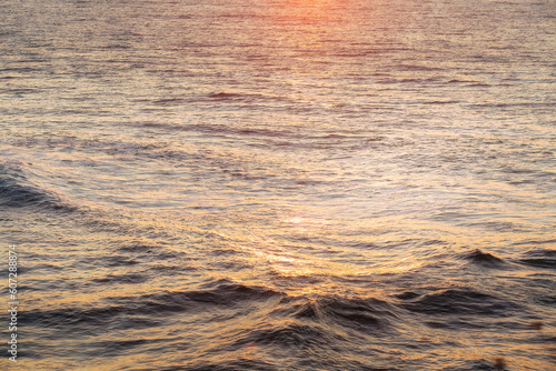 Water sea surface with waves lightened by the sun at sunset, background