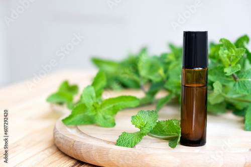Organic mint essential oil in small bottle and green leaf of peppermint on wooden board. Natural herbal cosmetic oil.