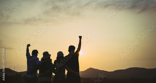 group of people with raised arms looking at sunrise on the mountain background. Happiness, success, friendship and community concepts.