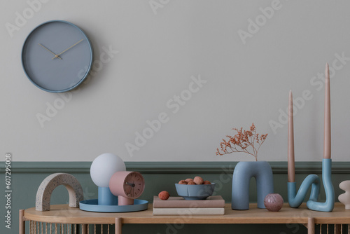 Warm composition of cozy living room interior with wooden sideboard, vase with dried flowers, books, blue lamp, clock, stylish sculpture and personal accessories. Home decor. Template. photo