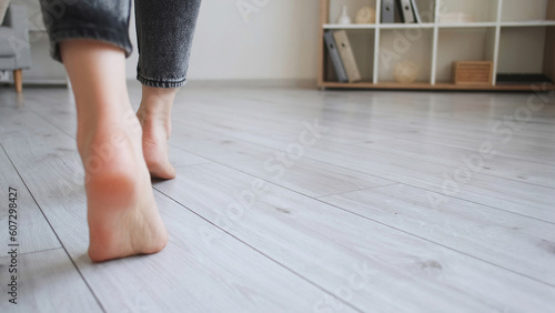 Floor heating. Home barefoot. Unrecognizable woman feet walking on warm laminated wood panels modern flat interior with copy space.