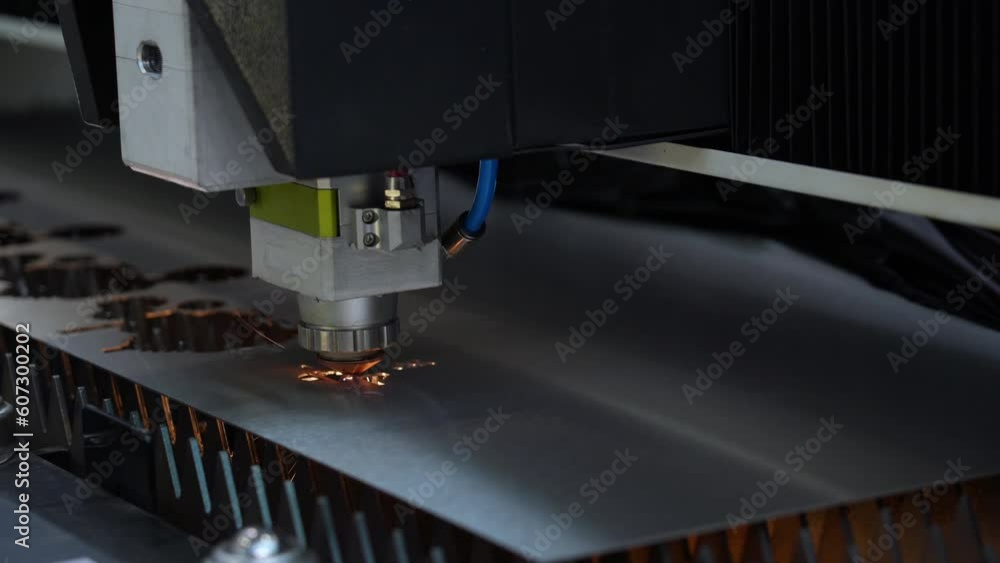 Robotic automatic laser cutting head with sparks cuts out the product along the contour of sheet metal on a high-precision CNC machine Robotic automatic laser cutting head with sparks cuts out the product along the contour of sheet metal on a high-precision CNC machine