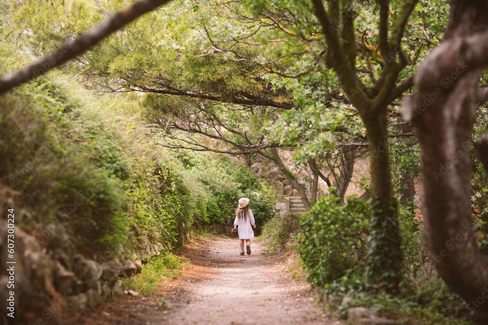 child girl runs along path of park in summer on vacation by sea. beautiful magic natural background with kids.