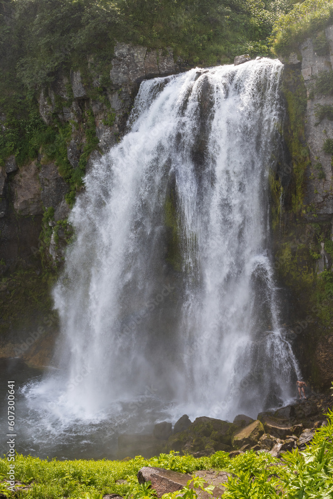 Big waterfall in a mountain gorge. Below, a man bathes under a waterfall. Travel on the Kamchatka Peninsula. Beautiful nature of the Russian Far East. Waterfall Spokoyny (Calm), Kamchatka Krai, Russia Big waterfall in a mountain gorge. Below, a man bathes under a waterfall. Travel on the Kamchatka Peninsula. Beautiful nature of the Russian Far East. Waterfall Spokoyny (Calm), Kamchatka Krai, Russia