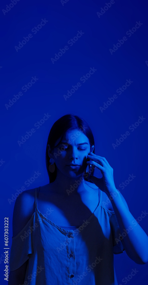 Mobile talking. Serious woman portrait. Focused neon color light girl smartphone call attentive expression listening information isolated on dark blue empty space background.