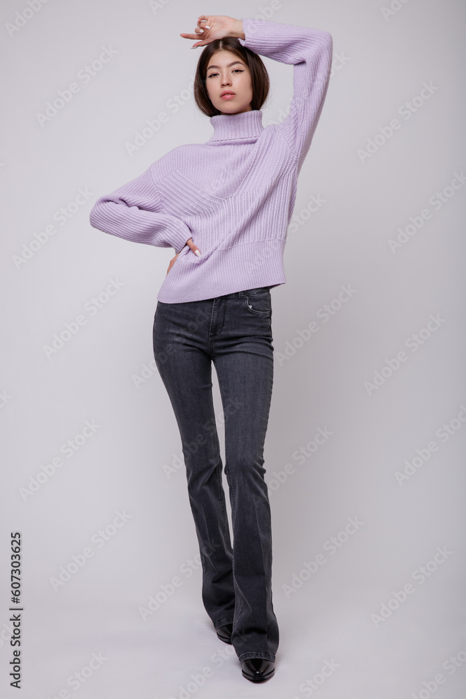 Fashion photo of a beautiful elegant young asian woman in a pretty pale purple, lilac, lavender sweater, blouse, black jeans, denim posing on white, soft gray background. Studio Shot. Slim figure. Fashion photo of a beautiful elegant young asian woman in a pretty pale purple, lilac, lavender sweater, blouse, black jeans, denim posing on white, soft gray background. Studio Shot. Slim figure.