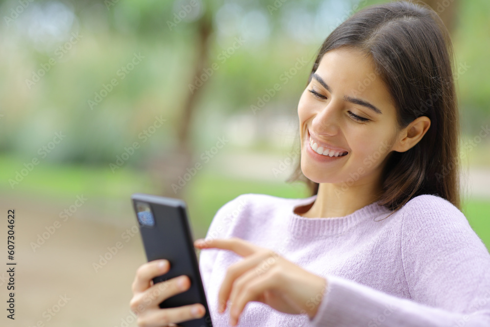 Happy woman is using cell phone in a park Happy woman is using cell phone in a park