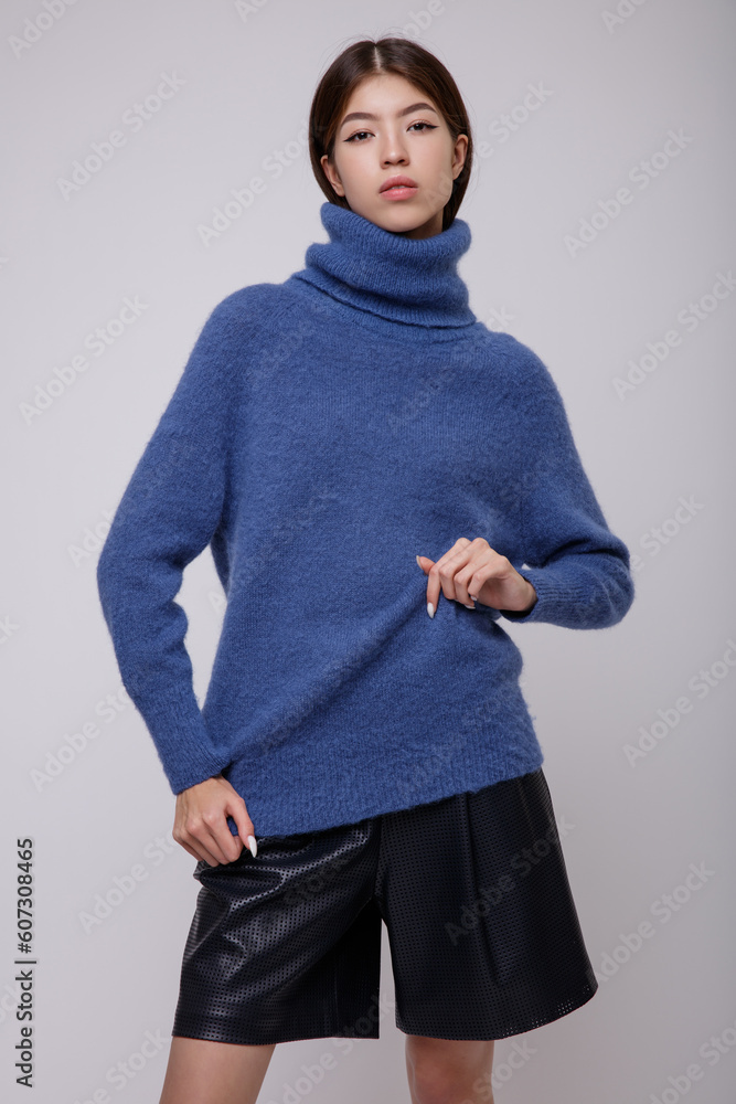 Fashion photo of a beautiful elegant young asian woman in a pretty blue sweater, blouse, black leather shorts posing on white, soft gray background. Studio Shot, portrait. Slim figure. Fashion photo of a beautiful elegant young asian woman in a pretty blue sweater, blouse, black leather shorts posing on white, soft gray background. Studio Shot, portrait. Slim figure.