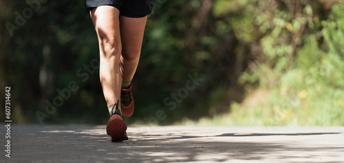 Woman runs in the forest on a rural asphalt road, athletic pair of legs running