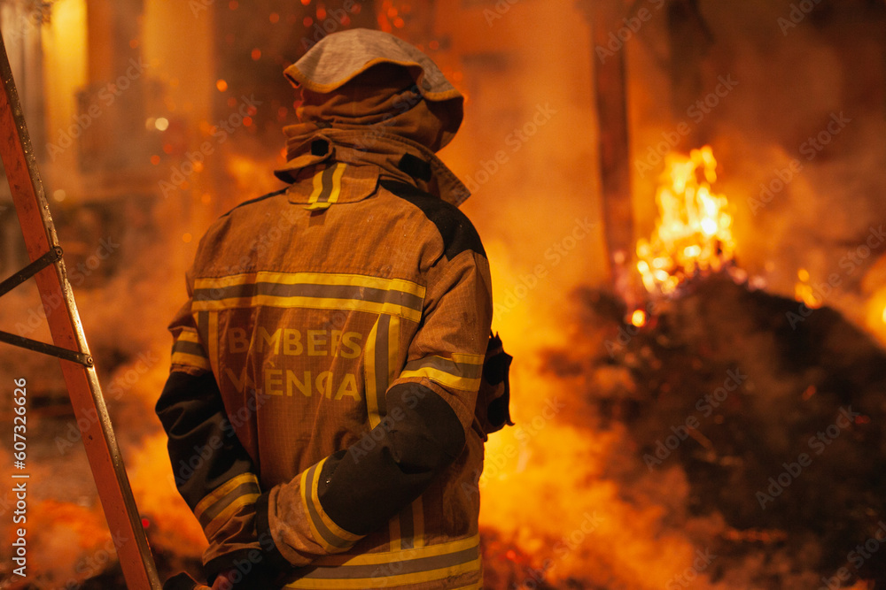 Firefighter closeup from behind standing in from of the fire working. Firemen fighting the flame. Firefighter closeup from behind standing in from of the fire working. Firemen fighting the flame.
