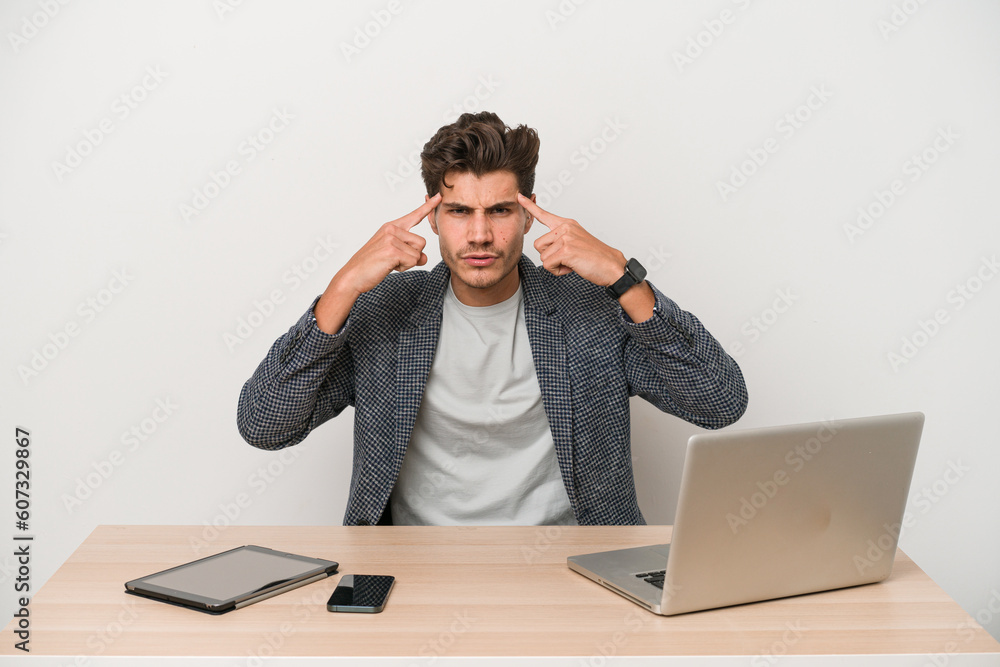 Young entrepreneur man working with a laptop isolated focused on a task, keeping forefingers pointing head. Young entrepreneur man working with a laptop isolated focused on a task, keeping forefingers pointing head.
