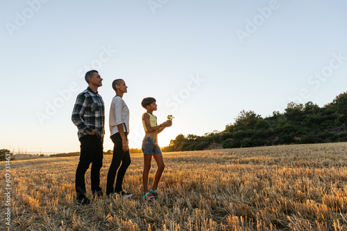 Family with a plant while standing outdoors in the field at sunset.